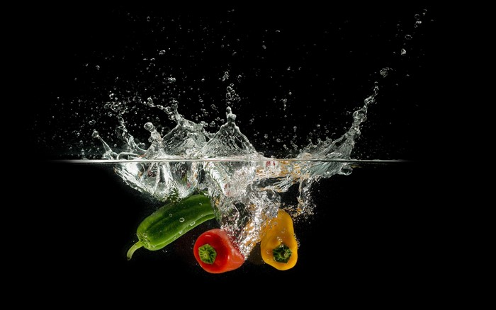 Bell peppers splashing into water on black background