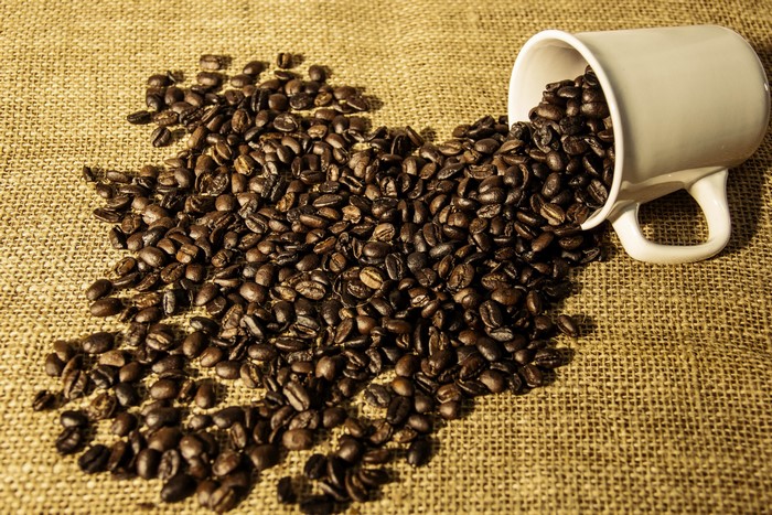 Coffee beans spilled from a mug onto burlap