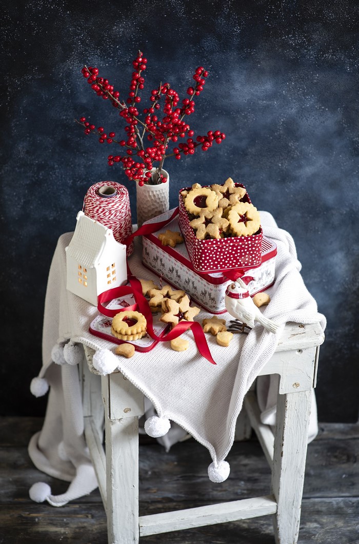 Christmas cookies in a tin with red berries and a white house lantern