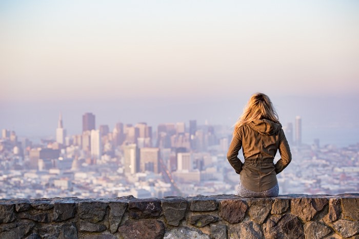 Blonde girl sitting on stone wall overlooking city
