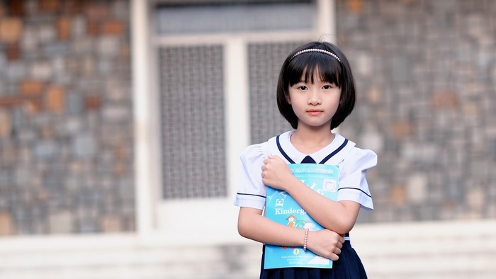 Young Schoolgirl Holding a Blue Book Outdoors