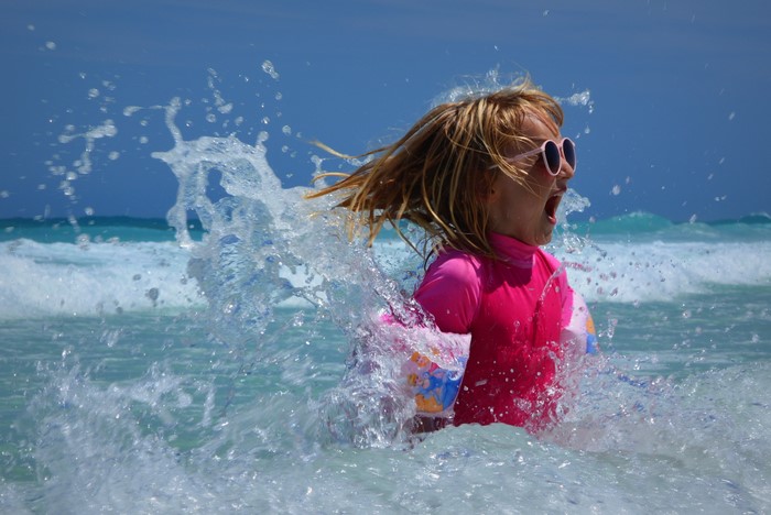 Girl in pink swimsuit and sunglasses in a water splash