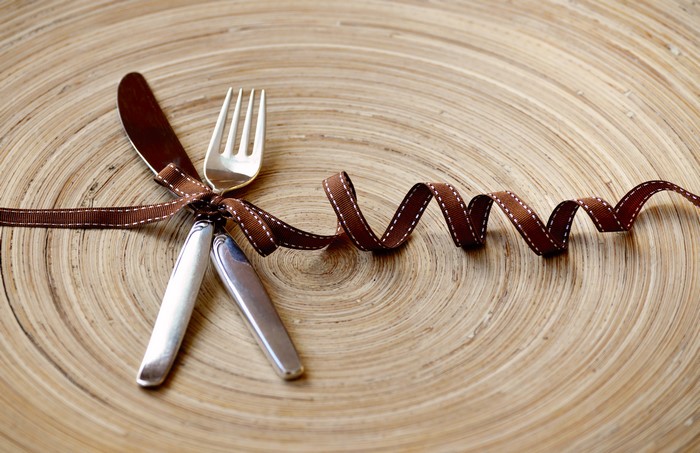 Knife and fork tied with ribbon on wooden plate