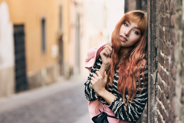 Redhead girl leaning against a brick wall