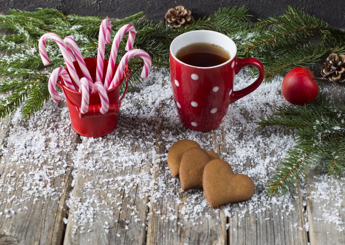 Christmas candy canes, mug of tea, and heart cookies on wood