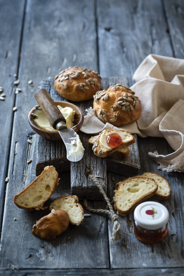 Buns with sunflower seeds, butter, jam, and bread slices on wood
