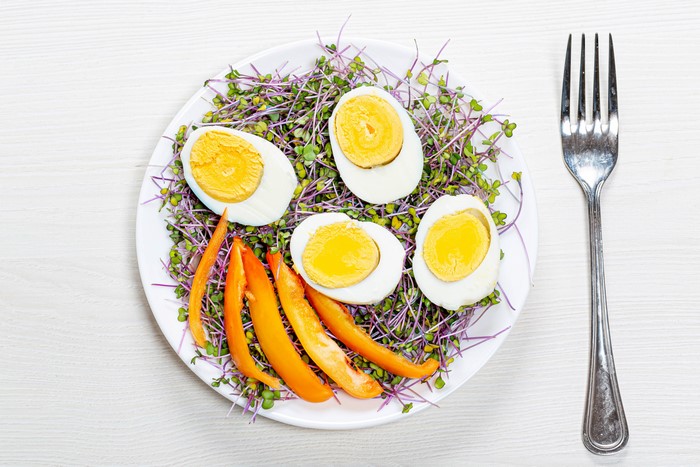 Hard-boiled eggs and bell pepper strips on sprouts with fork
