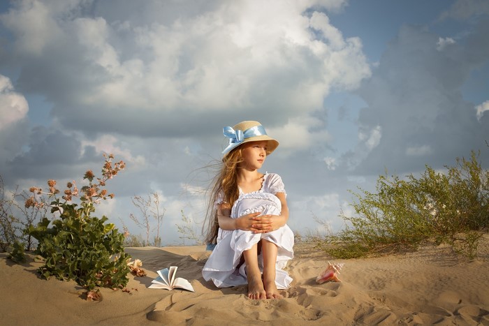 Girl in a hat and dress on sand with book and shell