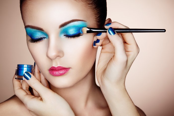 Woman applying blue eyeshadow with makeup brush