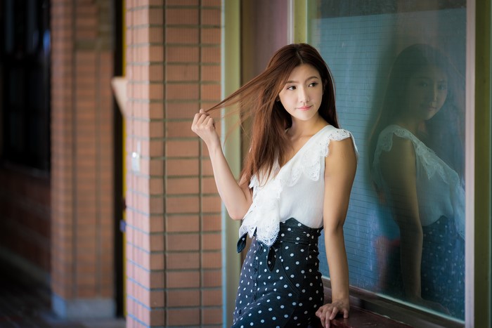 Asian woman with brown hair posing near a window