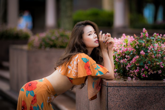 Asian woman in floral outfit posing near flowers
