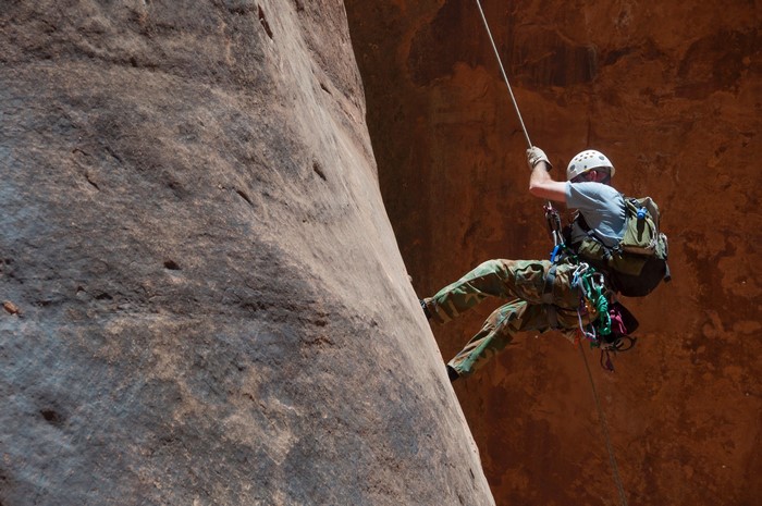 Man rappelling down a rocky cliff face
