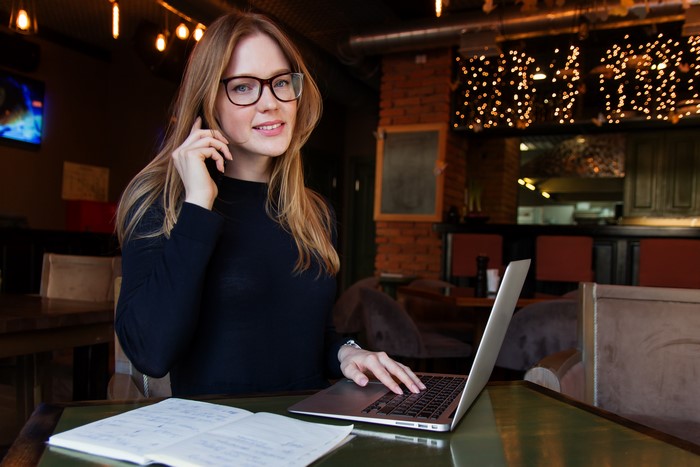 Woman with glasses on phone using laptop