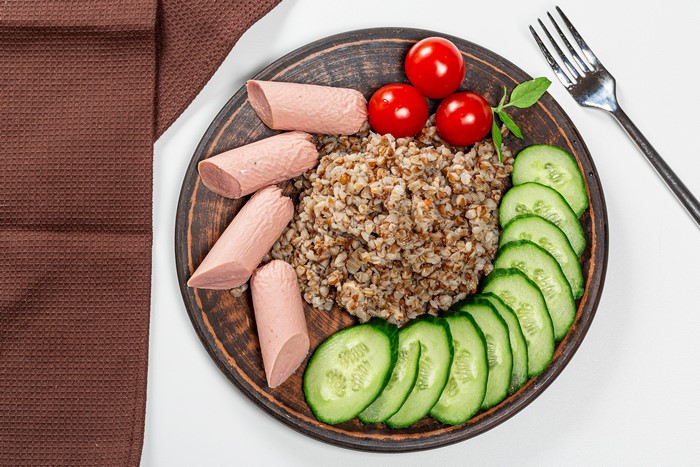 Buckwheat porridge with sausages, tomatoes, and cucumbers on a plate