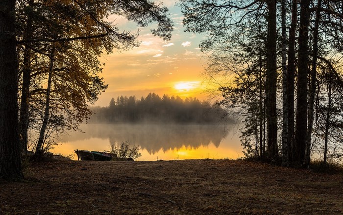 Sunrise over a foggy lake with boats on the shore