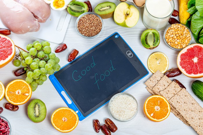 Good food written on a digital tablet surrounded by fruits and grains