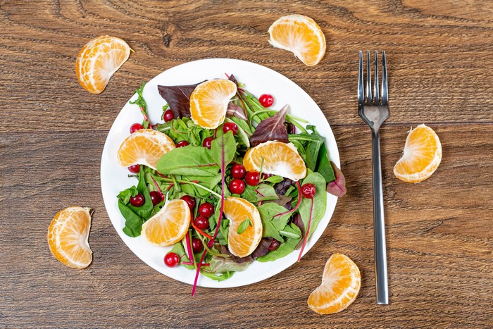 Salad with mandarin slices and berries on a plate with a fork