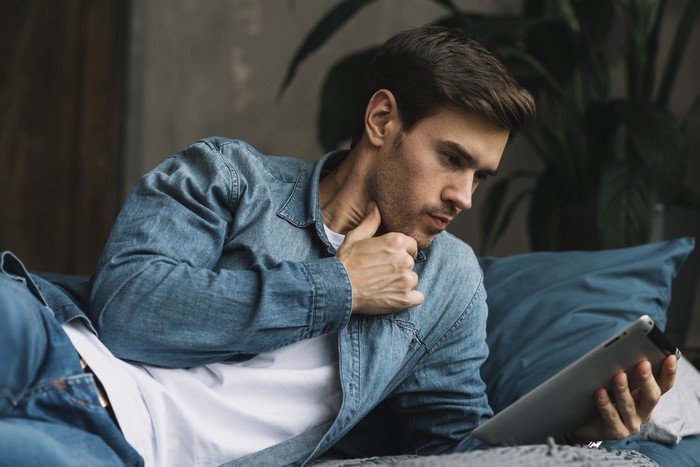 Man in denim shirt using tablet on bed