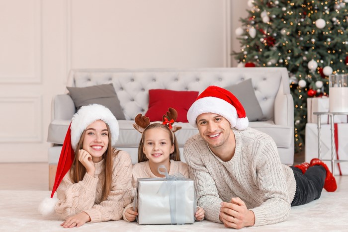 Family in Santa hats with gift by Christmas tree