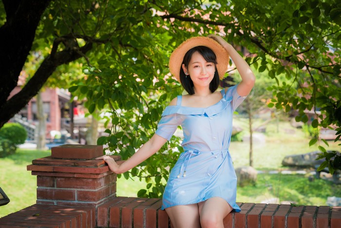 Asian woman in blue dress and straw hat sitting outdoors