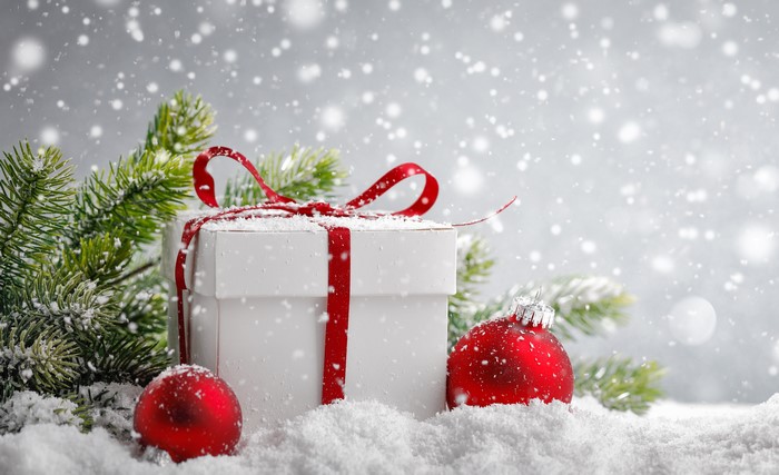 Christmas gift box with red ribbon and ornaments in snow