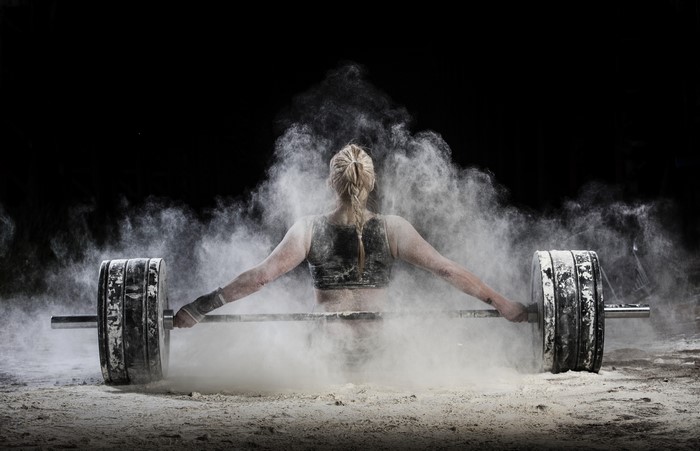 Woman lifting barbell covered in chalk