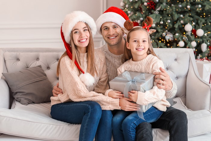 Family in Santa hats with Christmas tree and gift