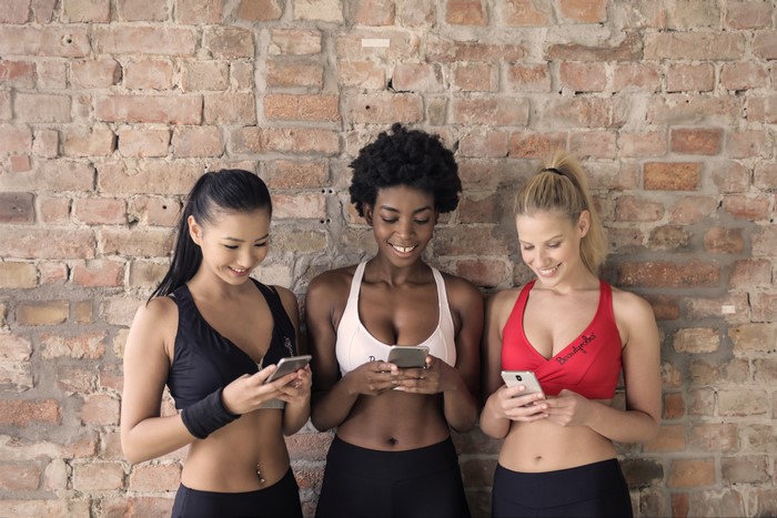 Three women in athletic wear looking at smartphones