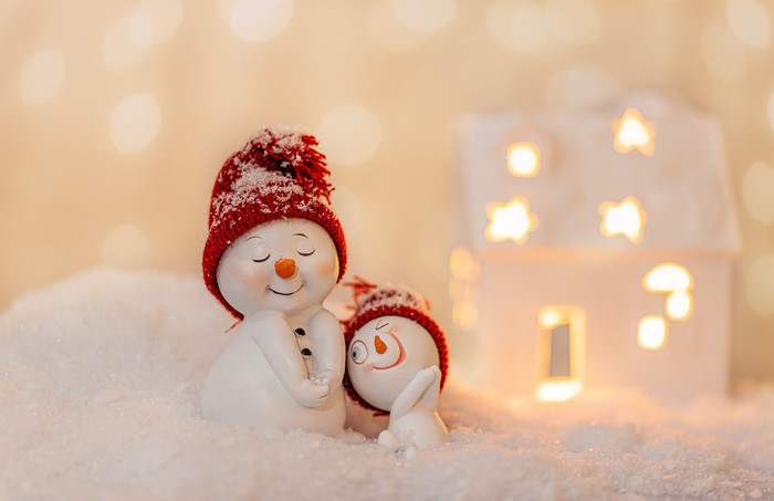 Two snowmen in red hats with bokeh lights and a house