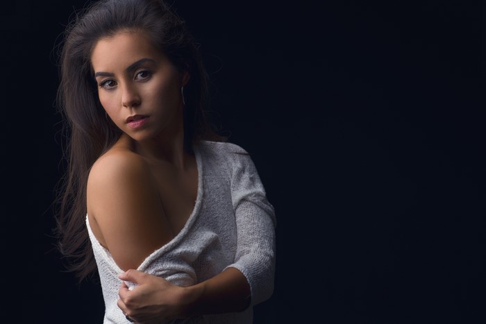 Brunette girl in sweater with hands on black background