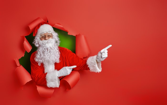 Santa Claus pointing through torn red background