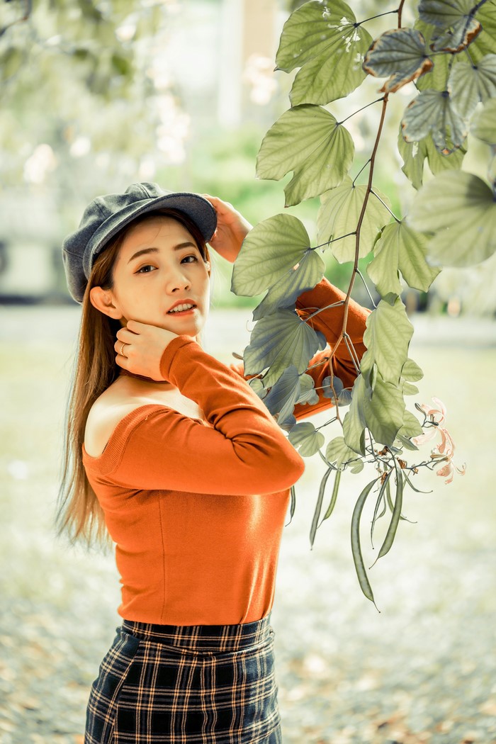Asian woman in a hat and orange top with plaid skirt