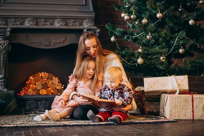 Mother reading a book to children by Christmas tree