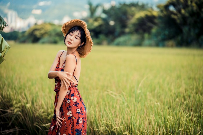 Asian woman in a straw hat and floral dress in a field