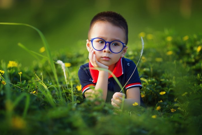 Asian boy with glasses lying in grass
