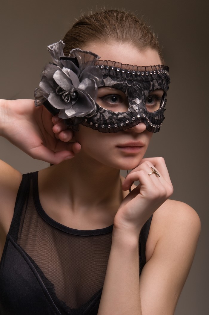 Woman wearing a black lace masquerade mask with a flower