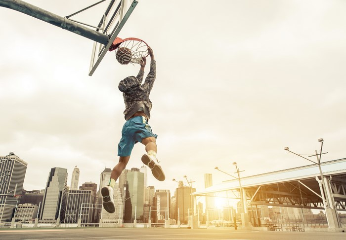Man dunking a basketball in a city