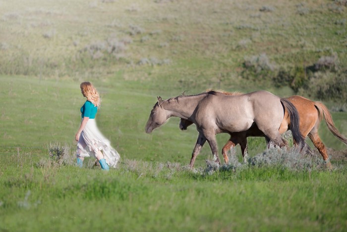 Blonde girl walking with horses in a grassy field