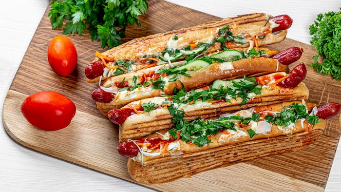 Four hot dogs with toppings on a wooden board