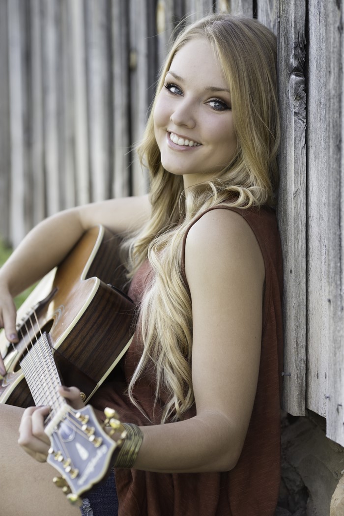 Blonde girl with guitar leaning on a fence