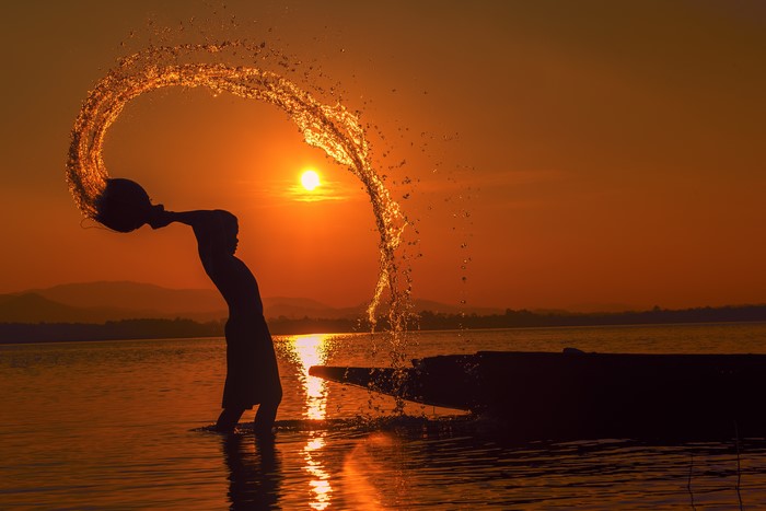 Silhouette of a boy splashing water at sunset