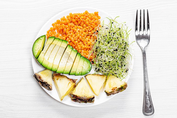 Plate of lentils, avocado, sprouts, and pineapple with fork