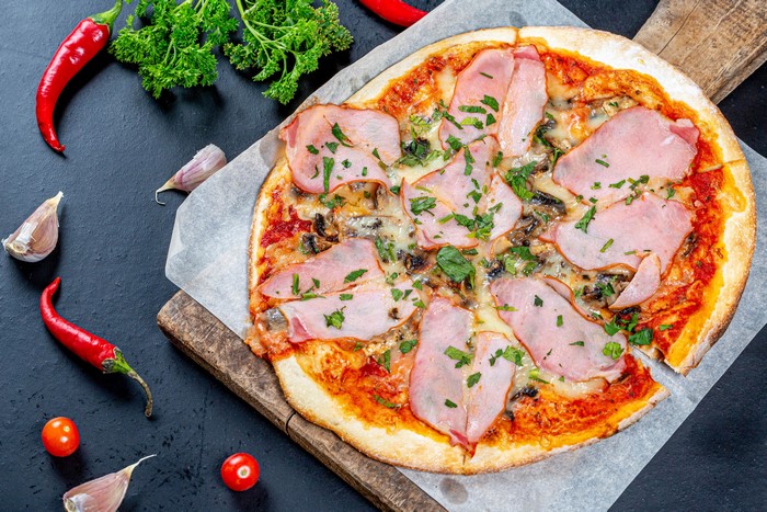 Pizza with Ham, Chili Peppers, and Garlic on Cutting Board