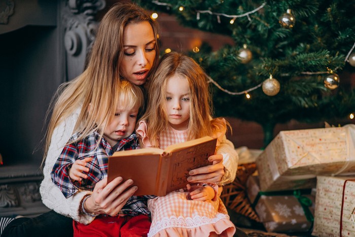 Mother reading a book to children by Christmas tree