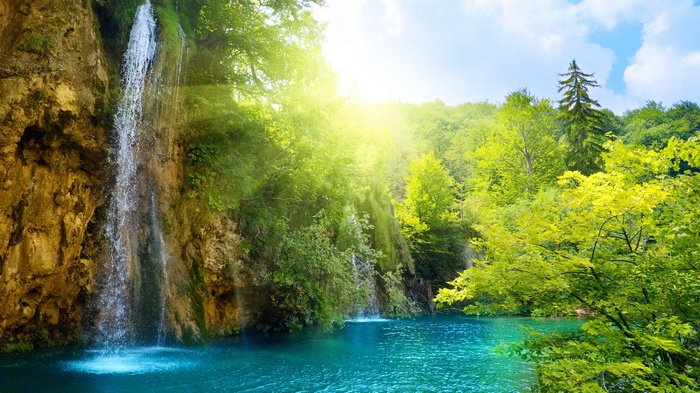 Waterfall cascading into a turquoise lake surrounded by lush green forest