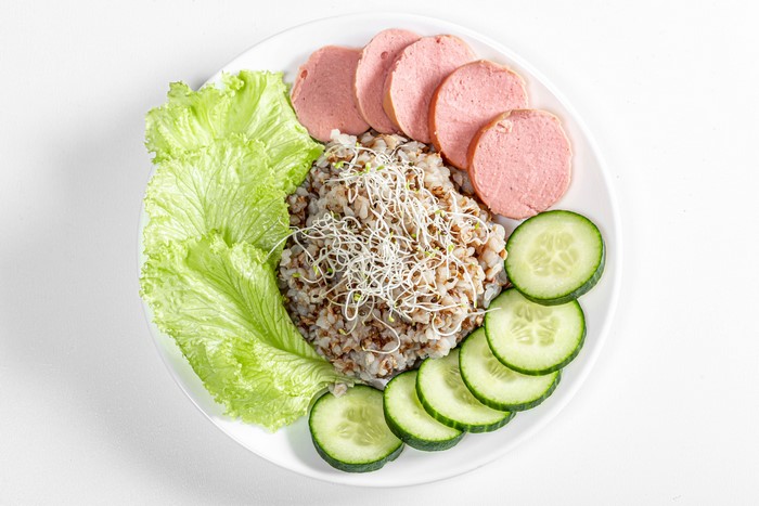 Buckwheat porridge with sausage, lettuce, and cucumber on a plate
