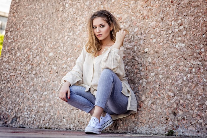 Woman in casual clothes squatting against a wall