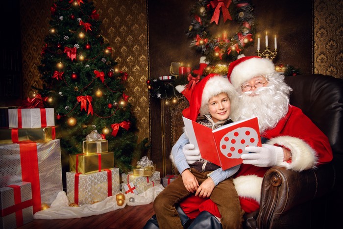 Santa Claus reading a book with a boy near a Christmas tree