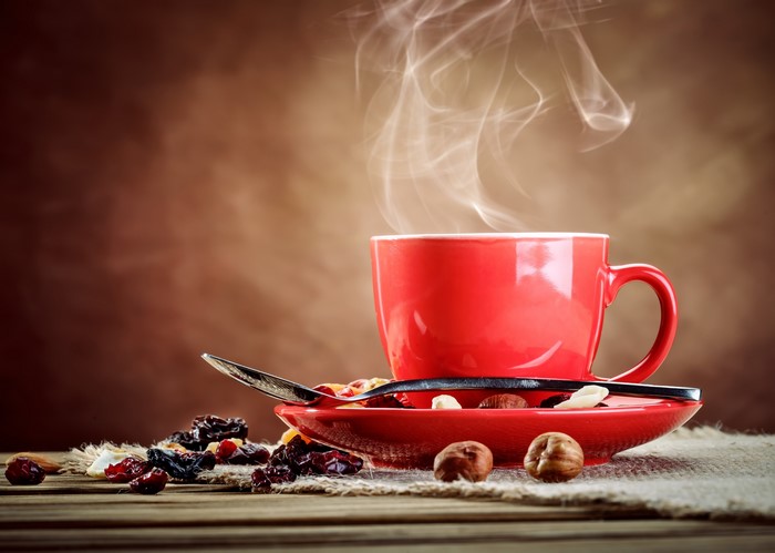 Red coffee cup with steam, saucer, spoon, and dried fruit