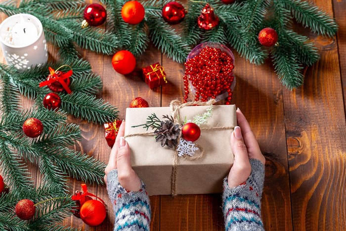 Hands holding a Christmas gift surrounded by decorations